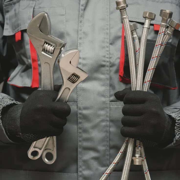 A plumber holding wrenches and braided water hoses