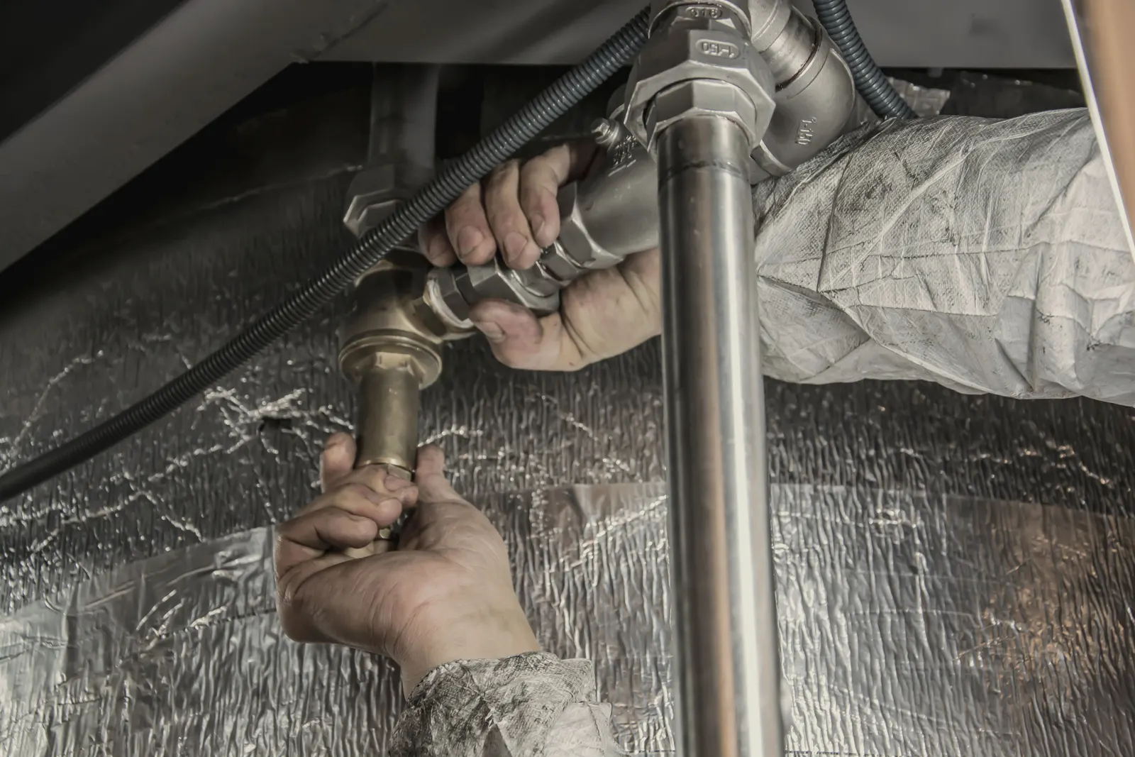 Hands tightening a brass fitting on a water pipe