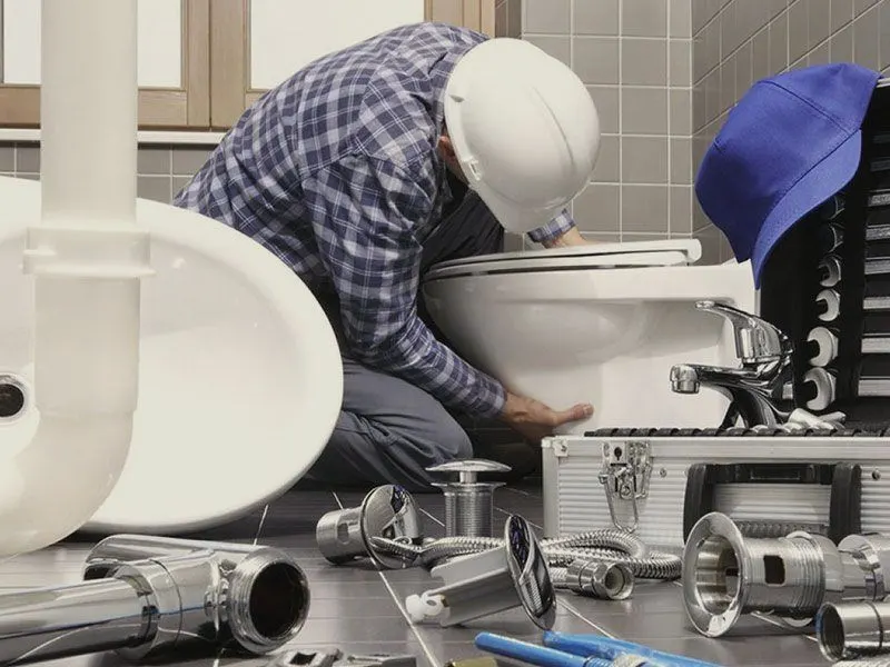 A plumber in a hard hat installing a toilet