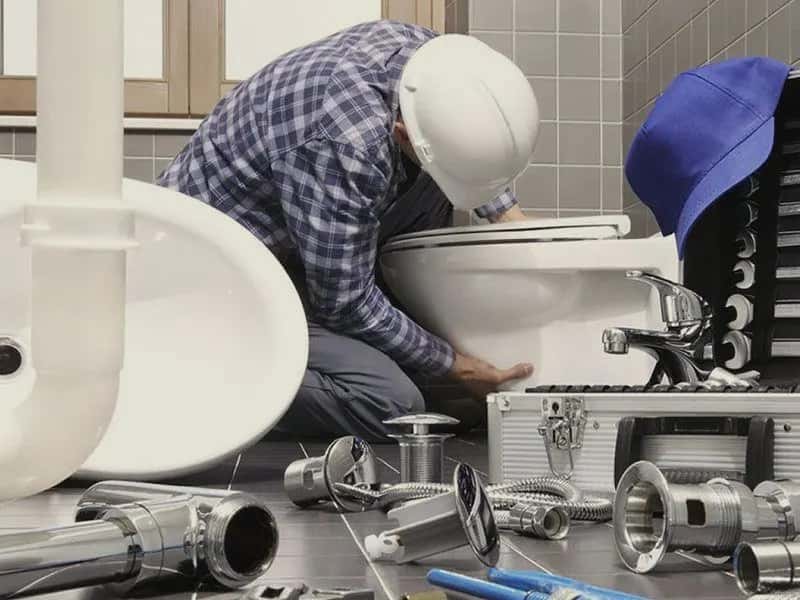 A plumber in a hard hat installing a toilet